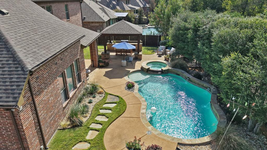 Backyard featuring a custom swimming pool with integrated spa, concrete patio, covered pavilion, and stone stepping stones set within a manicured lawn