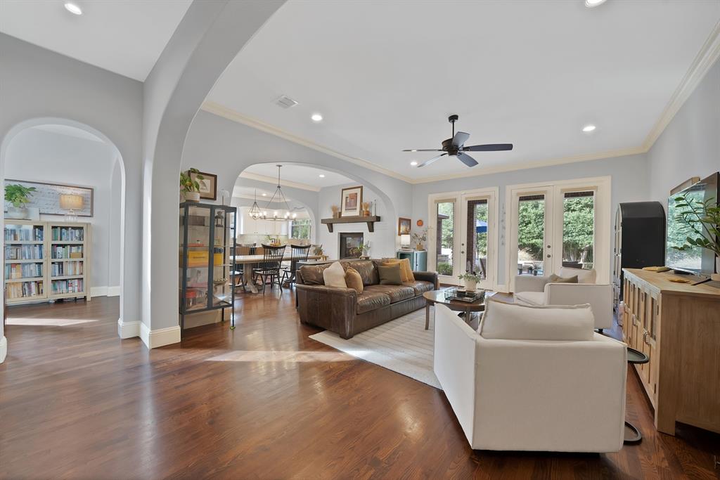 Open-concept living space featuring wood-finish flooring, recessed lighting, architectural arched doorways, a fireplace with a wood mantel, and multiple sets of glass-paned double doors