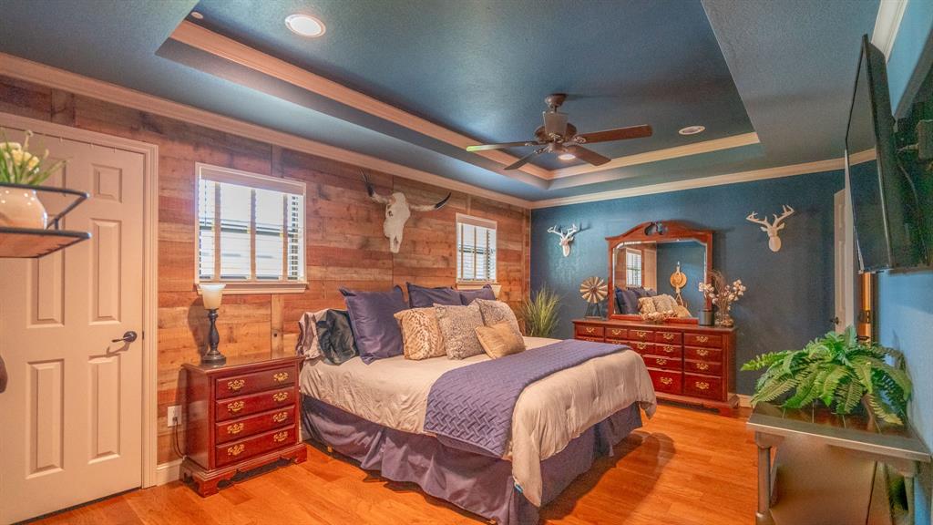Primary bedroom with wood flooring and a wood accent wall, trayed ceiling and recessed lighting
