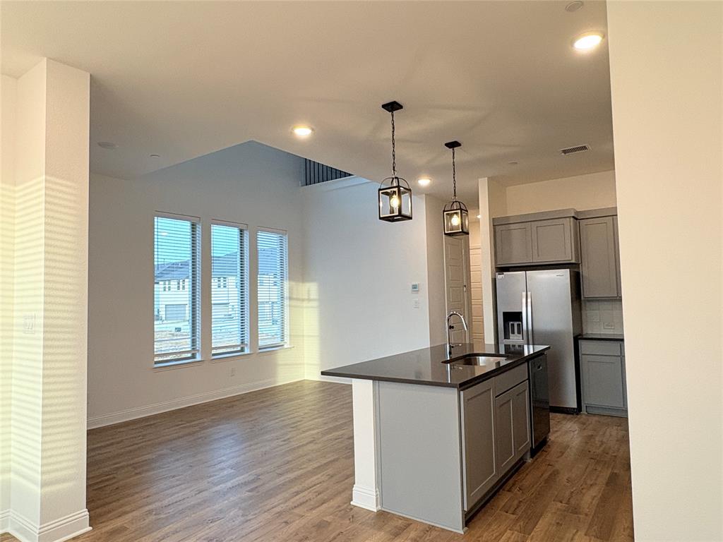 Kitchen featuring grey shaker-style cabinetry, stainless steel appliances, a dark-surface island with an integrated sink, wood-finish flooring, and pendant lighting Kitchen featuring grey shaker-style cabinetry, stainless steel appliances, a dark-surface island with an integrated sink, wood-finish flooring, and pendant lighting