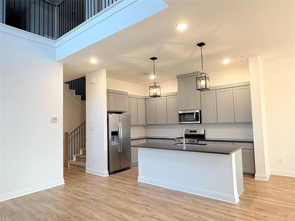 Kitchen featuring grey shaker-style cabinetry, dark stone countertops, an integrated island, stainless steel appliances, and wood-finish flooring