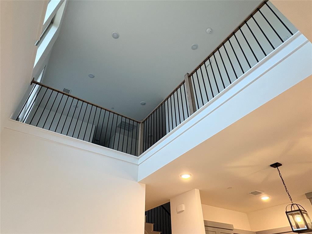 High-ceiling interior featuring a mezzanine overlook with black metal balusters, wooden handrails, recessed lighting, and a pendant fixture