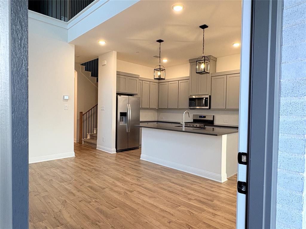 Kitchen featuring cabinetry with a gray finish, stone-surface island, stainless steel appliances, pendant lighting, and wood-finish flooring Kitchen featuring cabinetry with a gray finish, stone-surface island, stainless steel appliances, pendant lighting, and wood-finish flooring