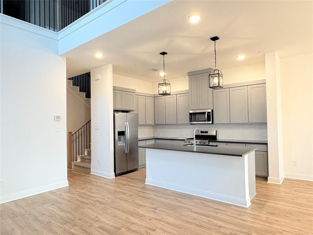 Kitchen featuring gray shaker-style cabinetry, stainless steel appliances, a center island with a stone-finish countertop, wood-finish flooring, and pendant lighting