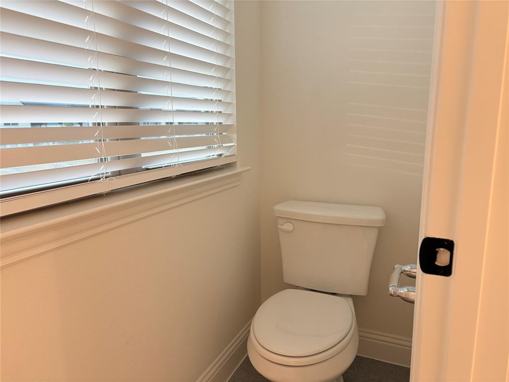 Water closet featuring a two-piece toilet, horizontal window blinds, and solid-surface flooring