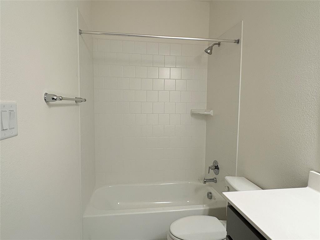 Bathtub and shower combination with white tile surround, chrome fixtures, built-in soap dish, and vanity with countertop