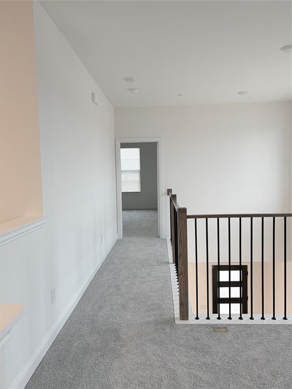 Neutral interior hallway featuring carpeted flooring, recessed lighting, and a staircase railing with wood posts and metal balusters