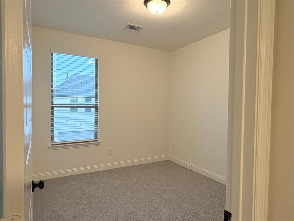 Neutral-toned interior space featuring light-colored wall paint, carpeted flooring, a single window with horizontal blinds, and a central ceiling-mounted light fixture