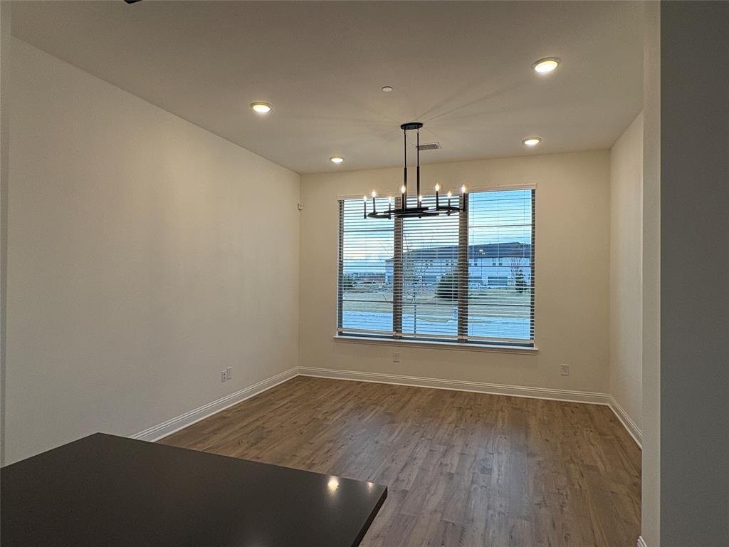 Room featuring wood-finish flooring, recessed lighting, a modern multi-arm chandelier, and a large multi-pane window with horizontal blinds Room featuring wood-finish flooring, recessed lighting, a modern multi-arm chandelier, and a large multi-pane window with horizontal blinds