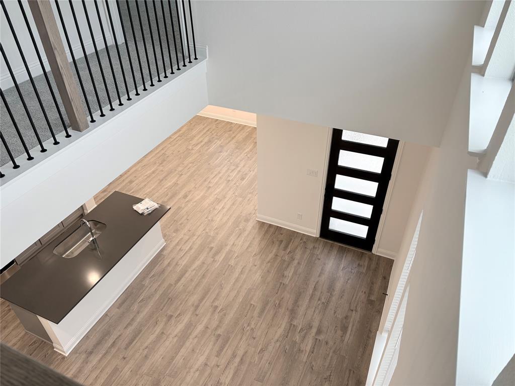 Double-height ceiling with wood-finish flooring, island featuring a built-in sink, and black-framed five-panel entry door with matte black stair balusters