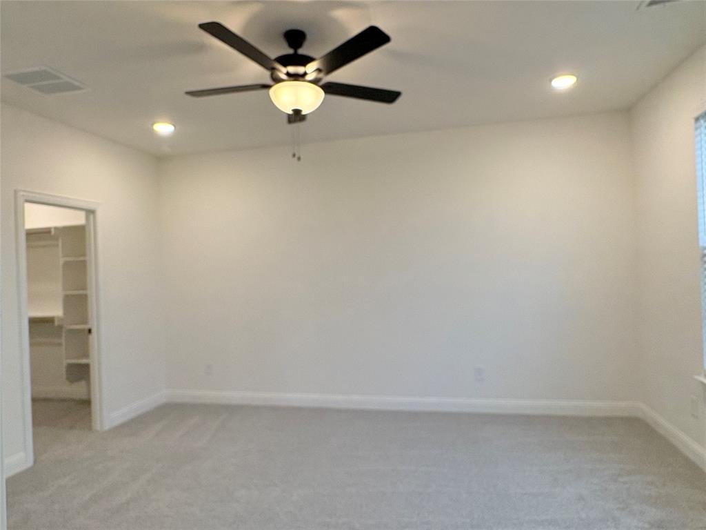 Neutral-toned carpeted flooring, multi-blade ceiling fan with integrated lighting, recessed ceiling lights, and walk-in storage area with built-in shelving