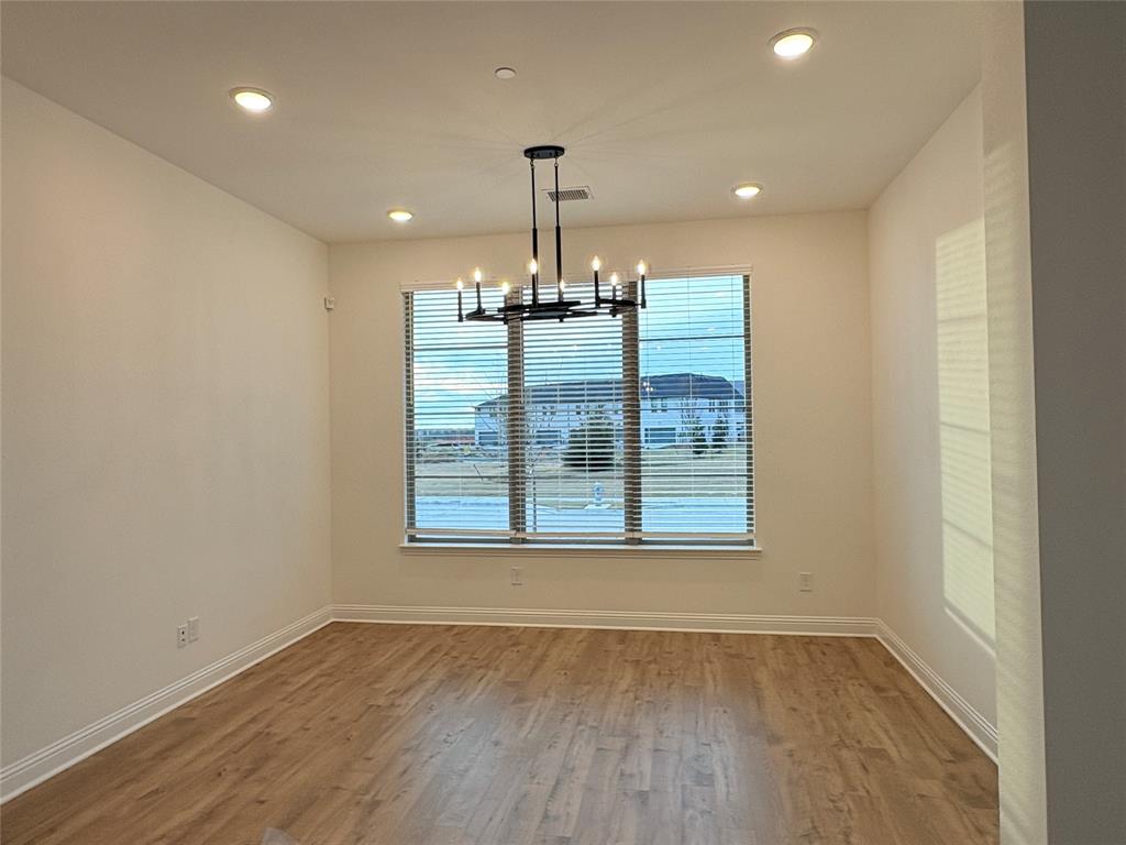 Room featuring wood-finish flooring, a tiered matte black chandelier, recessed lighting, and large windows with horizontal blinds Room featuring wood-finish flooring, a tiered matte black chandelier, recessed lighting, and large windows with horizontal blinds