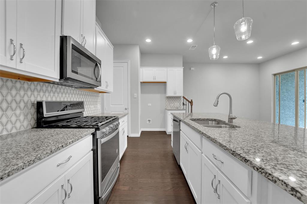Contemporary kitchen featuring white cabinetry, stainless steel appliances, granite countertops, and a patterned tile backsplash
