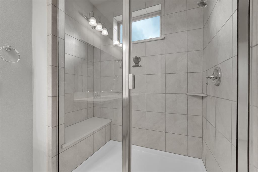 Glass-enclosed shower with tile surround, built-in bench, and chrome fixtures