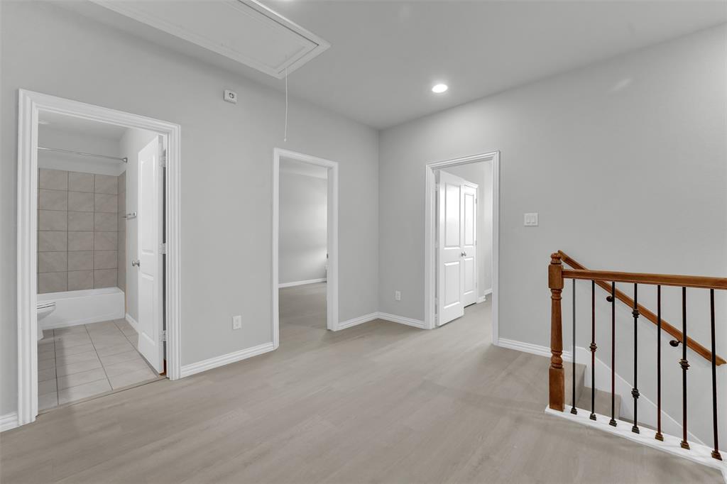 Light gray wood-finish flooring, recessed lighting, white trim, and a staircase with wood handrails and black metal balusters