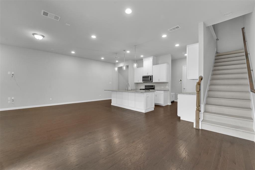 Open-concept living area featuring wood-finish flooring, recessed lighting, and a modern kitchen with white cabinetry, stainless steel appliances, and a tiled backsplash