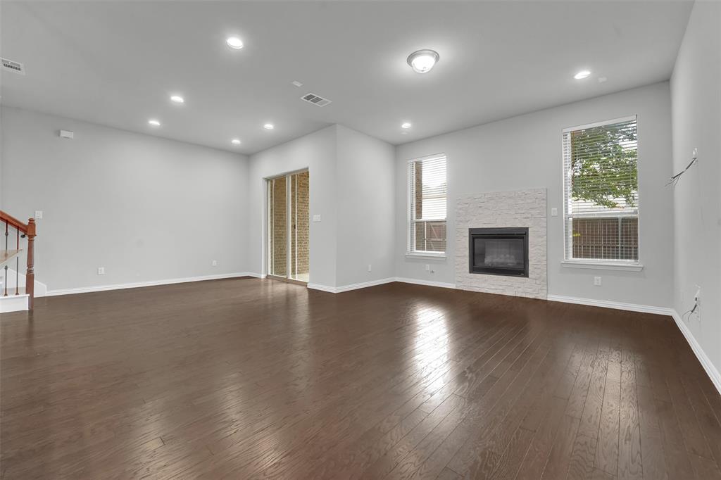 Spacious living area featuring wood-finish flooring, recessed lighting, and a fireplace with a textured stone surround