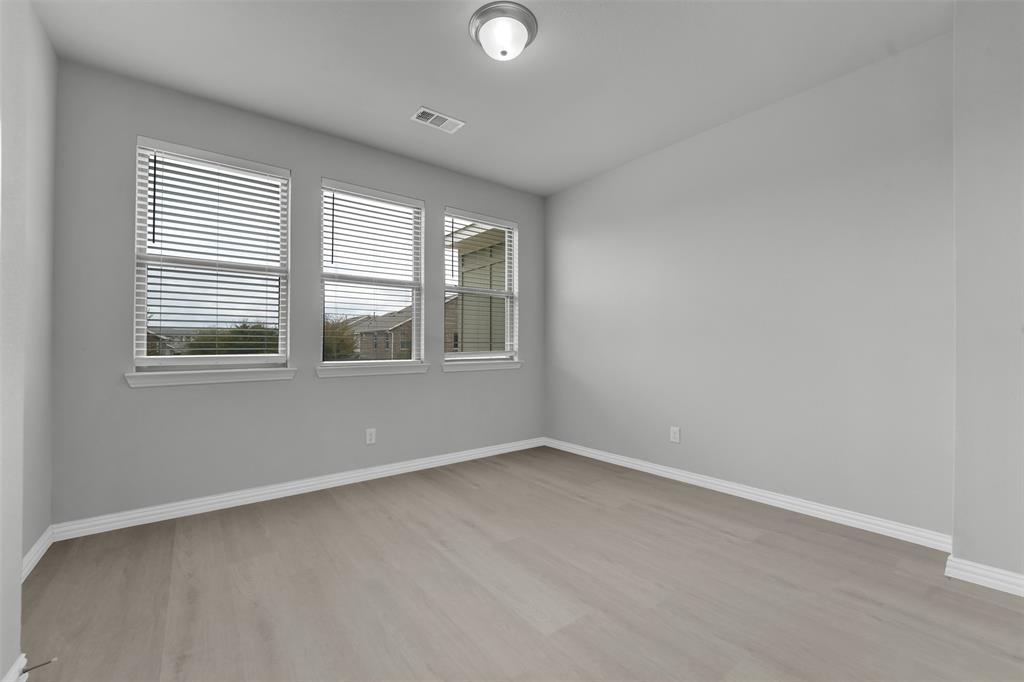 Light gray wood-finish flooring, multiple windows with blinds, and flush-mount ceiling light