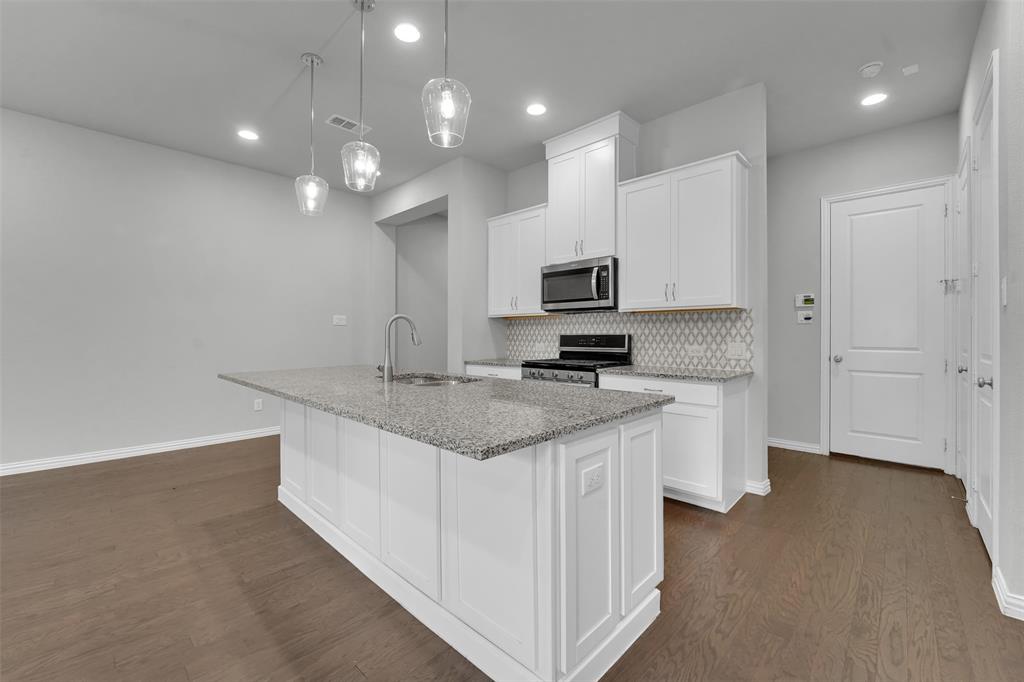 Kitchen featuring wood-finish flooring, a central island with a stone countertop, pendant lighting, white cabinetry, and a patterned tile backsplash