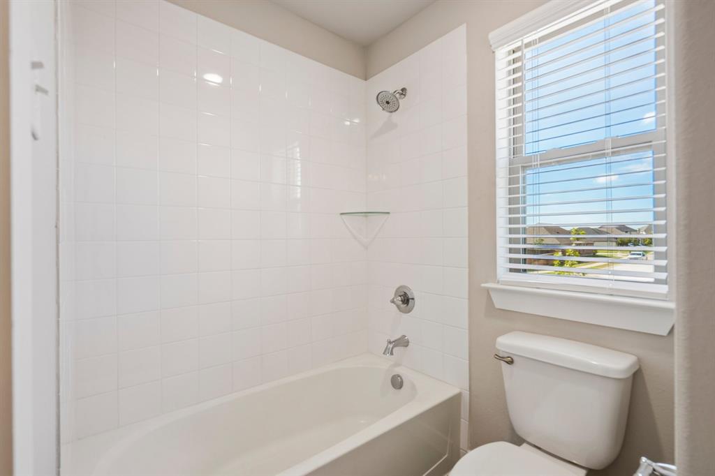 Full bathroom featuring a white tile shower surround, integrated glass corner shelf, chrome fixtures, and a single-hung window with horizontal blinds