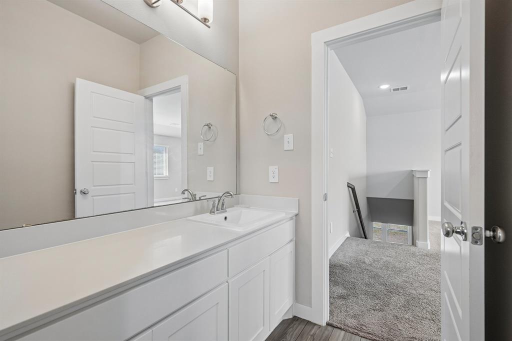 Bathroom featuring a white vanity cabinet, solid-surface countertop with an integrated basin, expansive wall-mounted mirror, polished chrome faucet, and three-bulb vanity lighting fixture