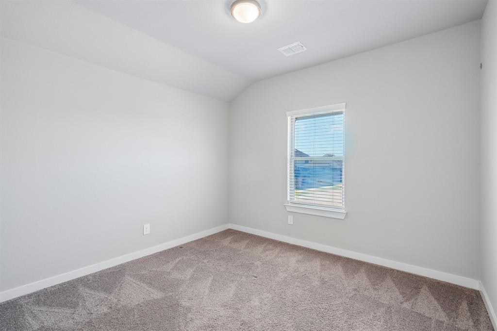 Neutral-toned interior featuring wall-to-wall carpeting, a single-pane window with horizontal blinds, and a vaulted ceiling with a flush-mount light fixture