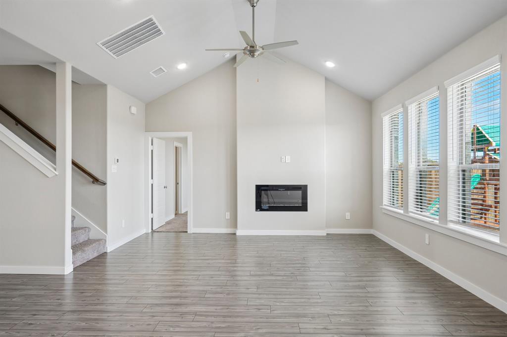 Vaulted ceilings featuring recessed lighting, a modern built-in wall fireplace, wood-finish flooring, and expansive windows with blinds