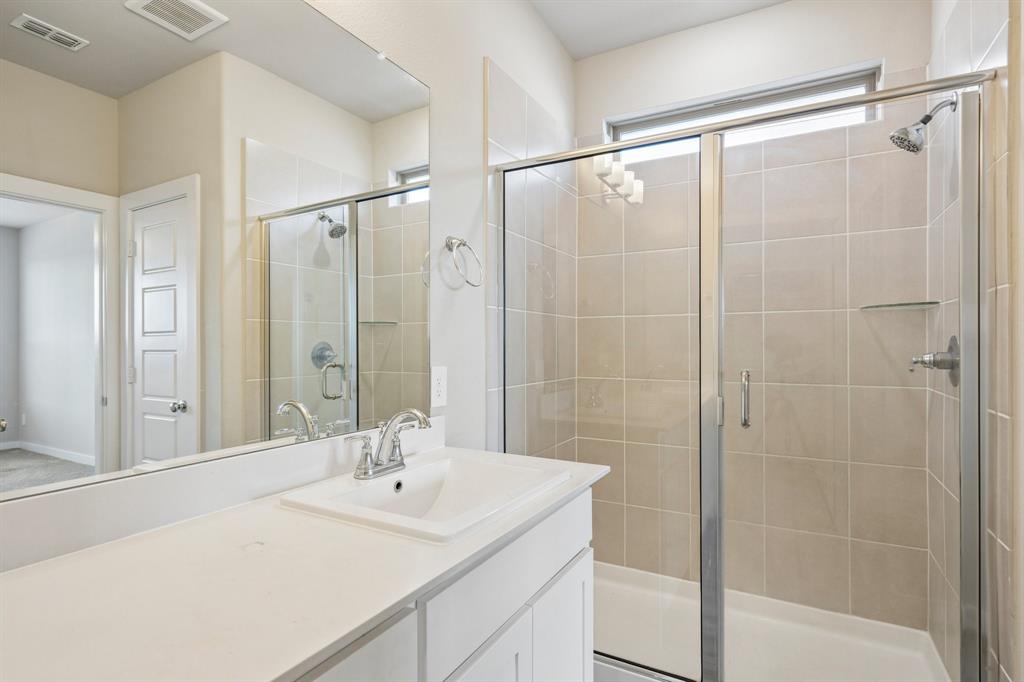 Bathroom featuring a white vanity with a composite countertop, an integrated rectangular sink, a large wall-mounted mirror, and a glass-enclosed shower with tiled walls