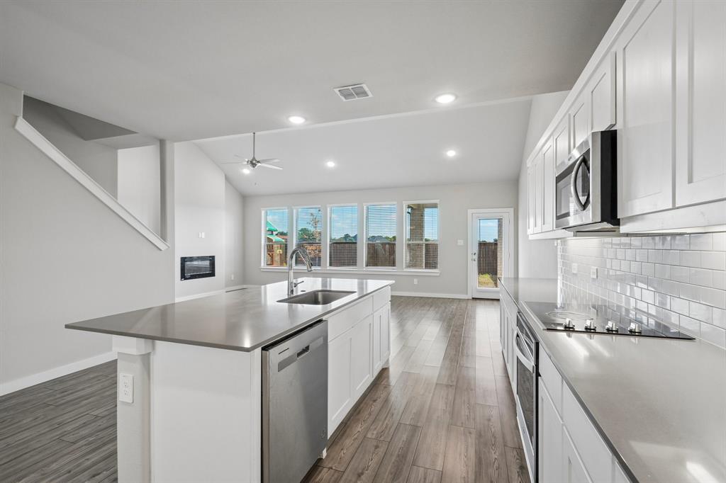 Kitchen featuring white cabinetry, quartz countertops, a subway tile backsplash, stainless steel appliances, and wood-finish flooring under vaulted ceilings
