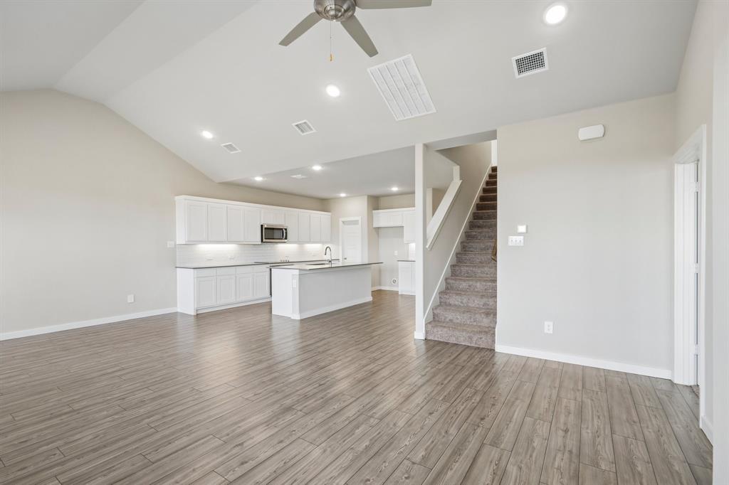 Vaulted ceilings featuring a ceiling fan, white cabinetry, a center island with a stone countertop, recessed lighting, and wood-finish flooring