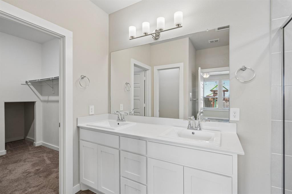 White dual-sink vanity with a solid surface countertop, four-light wall-mounted fixture, and full-width vanity mirror