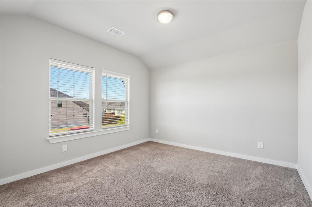 Neutral-toned interior room featuring wall-to-wall carpeting, vaulted ceilings, and dual windows with fitted blinds