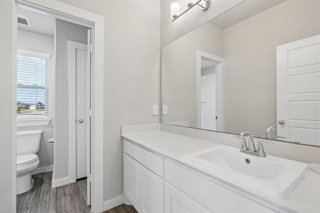 Bathroom featuring a white shaker-style vanity with a composite countertop, an undermount sink, a full-width wall mirror, and wood-finish flooring