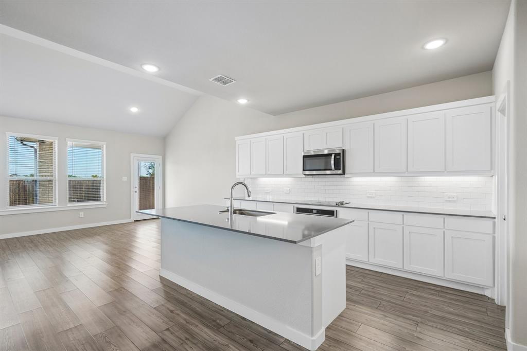 Kitchen featuring white shaker-style cabinetry, quartz countertops, a central island with an integrated sink, subway tile backsplash, and wood-finish flooring