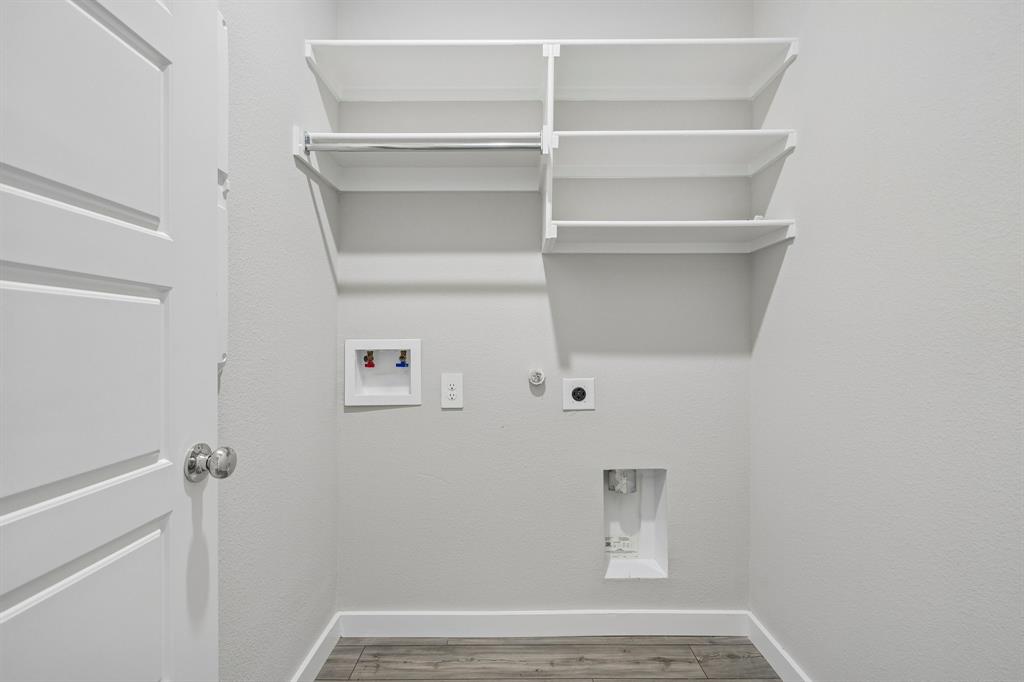 Utility space featuring wood-finish flooring, white shelving with integrated clothing rods, and dedicated water and electrical hookups