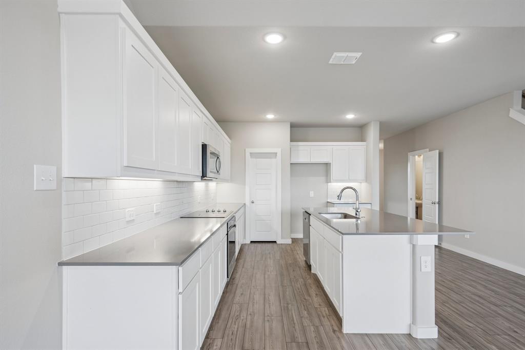 Kitchen featuring white cabinetry, quartz countertops, subway tile backsplash, stainless steel appliances, and wood-finish flooring