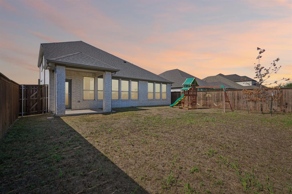 Rear exterior featuring a brick facade, covered patio, large windows, and perimeter wood fencing