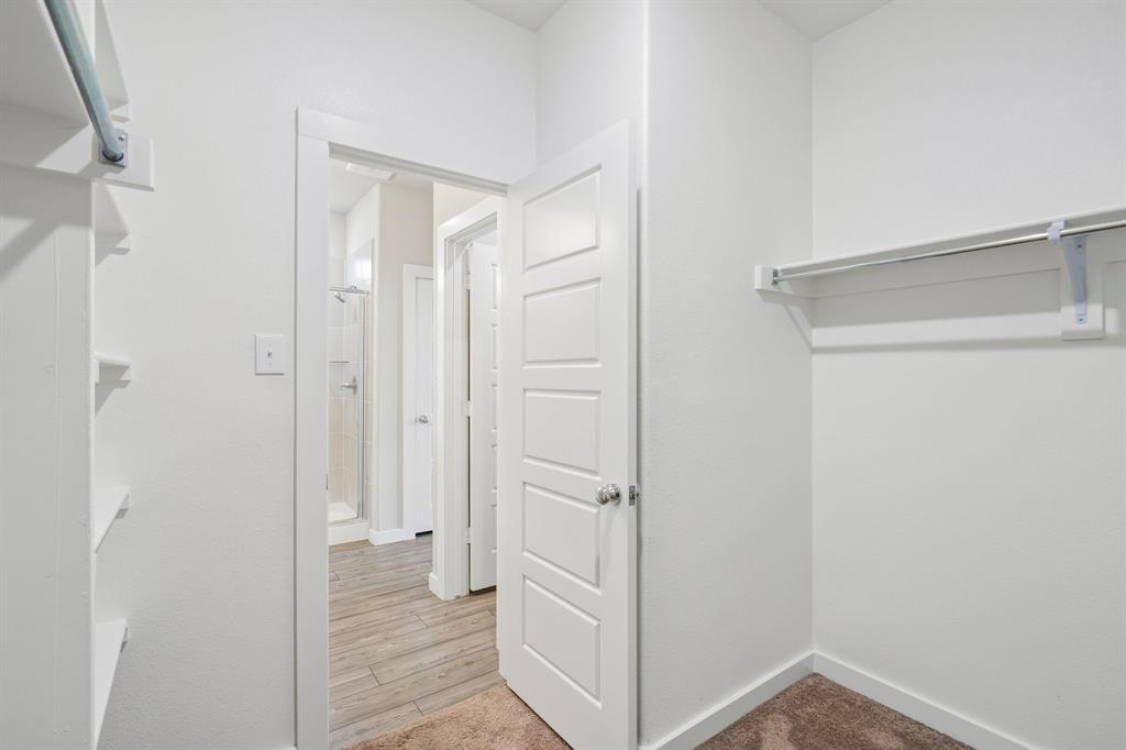 Walk-in closet featuring white built-in shelving, a hanging rod, a five-panel interior door, and neutral carpeting