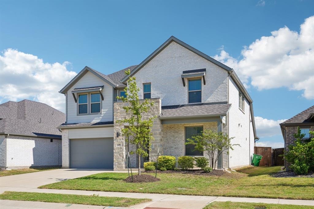 Two-story exterior featuring a brick and stone facade, gabled roofline, covered entryway, and attached garage