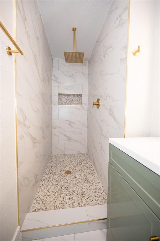 Walk-in shower featuring floor-to-ceiling stone-finish tile, pebble-stone flooring, an integrated tiled niche, a gold-tone rain-style shower head, and gold-tone trim