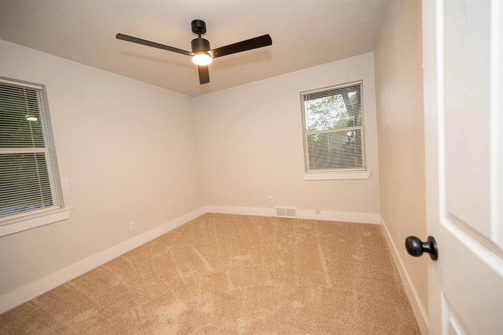 Neutral interior room featuring plush carpeting, a modern matte black ceiling fan with integrated lighting, and dual windows
