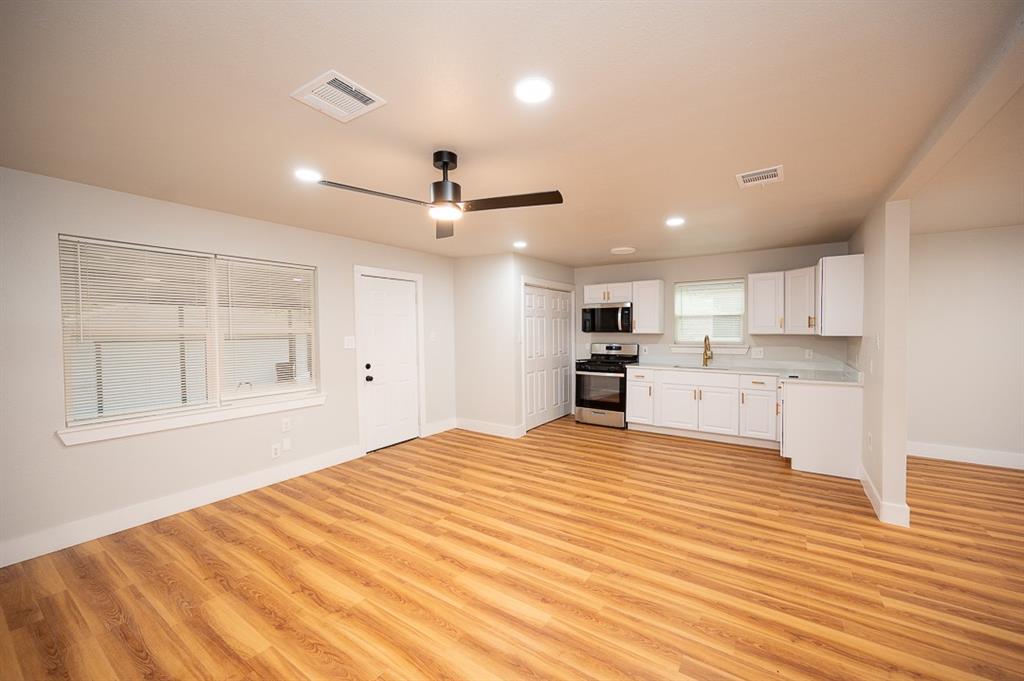 Open-concept interior featuring wood-finish flooring, white shaker cabinetry, stainless steel appliances, recessed lighting, and a modern ceiling fan