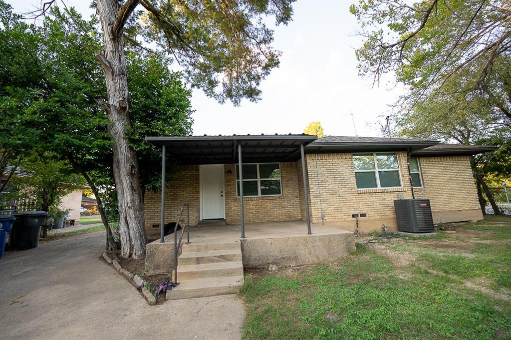Exterior featuring a light brick facade, covered concrete front porch with metal supports, and mature trees