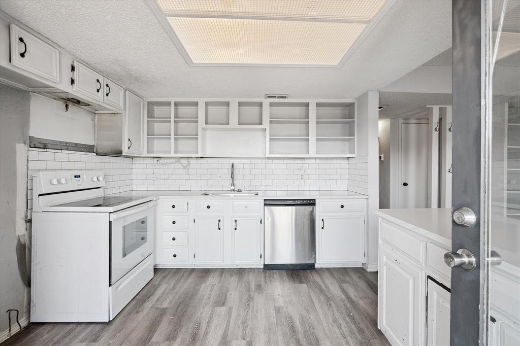 Kitchen featuring white shaker-style cabinetry, open shelving, white subway tile backsplash, stainless steel dishwasher, and wood-finish flooring