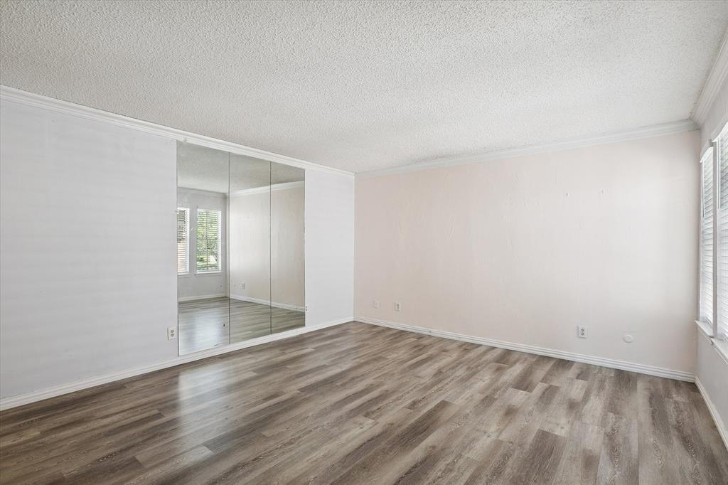 Interior space featuring wood-finish flooring, floor-to-ceiling mirrored wardrobe doors, textured ceilings, and crown molding