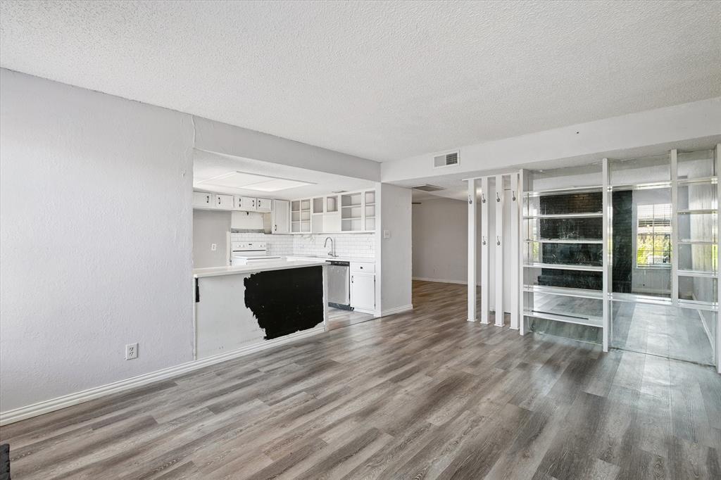 Open-concept interior featuring wood-finish flooring, white cabinetry, a kitchen peninsula, and decorative floor-to-ceiling room partition shelving