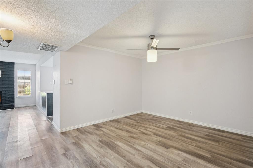 Interior space featuring wood-finish flooring, a ceiling fan with integrated lighting, textured ceiling, and a painted brick fireplace surround