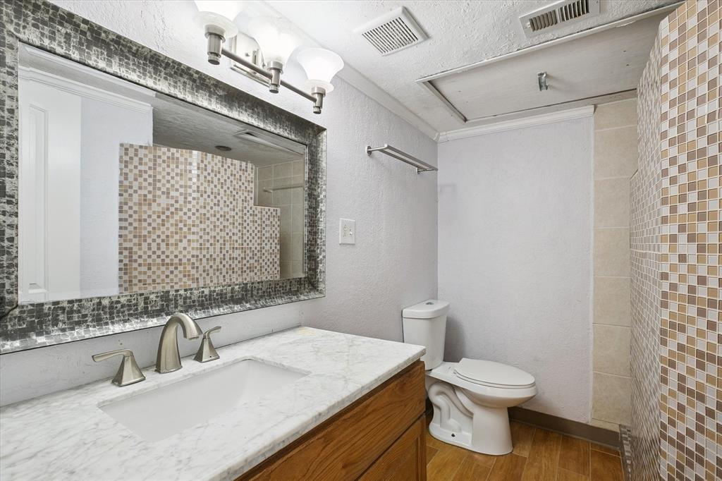 Bathroom featuring a vanity with a light-toned stone countertop, undermount sink, multi-tone mosaic tile backsplash, framed wall mirror, and wood-finish flooring