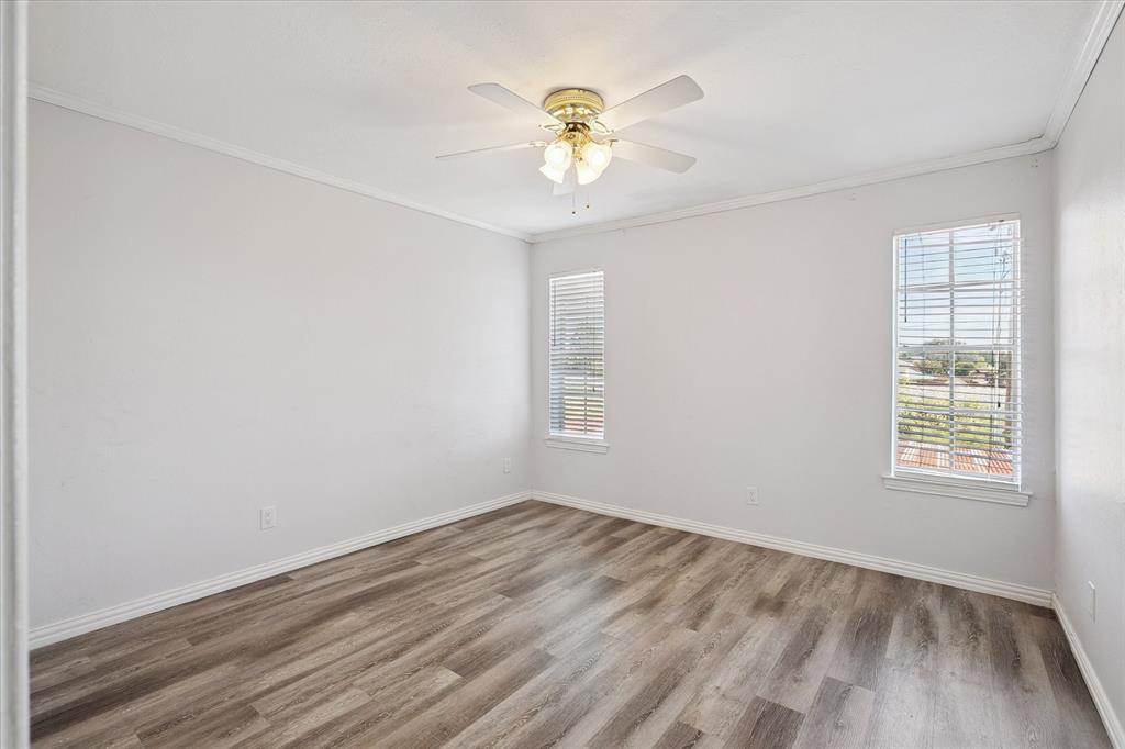 Room with wood-finish flooring, neutral wall paint, dual windows with installed blinds, and a multi-blade ceiling fan with integrated light fixture