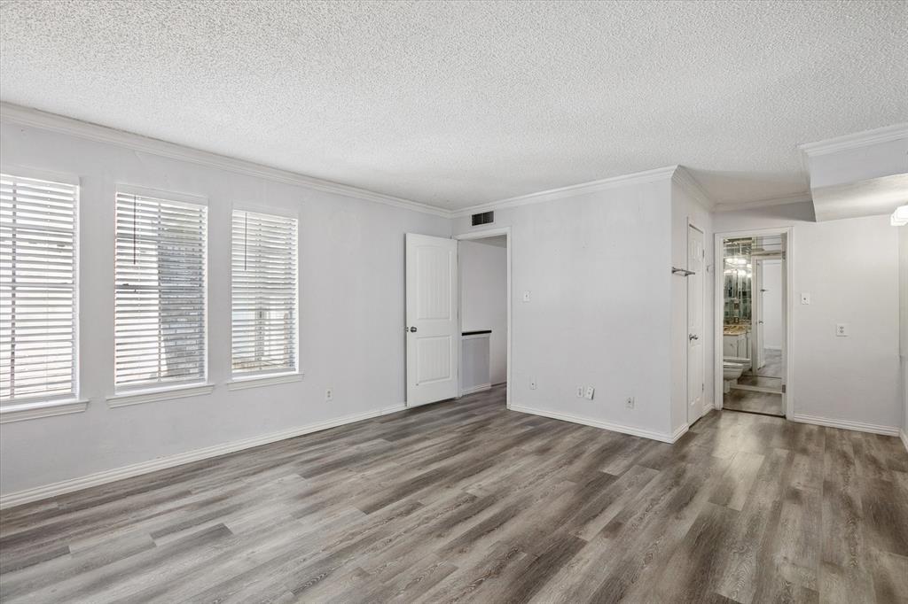 Neutral-toned interior featuring wood-finish flooring, crown molding, and windows fitted with white blinds